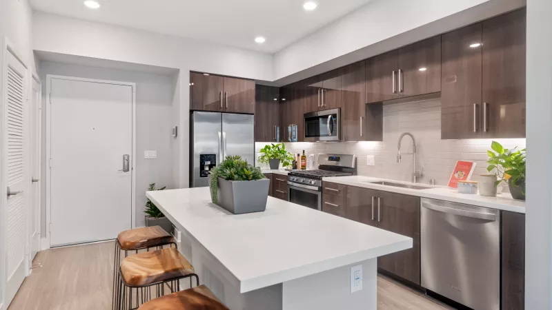 Modern kitchen with dark wood cabinets, stainless steel appliances, white island, and three wooden bar stools.