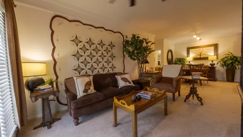 Cozy living room with a brown sofa, large geometric upholstered wall art, wooden coffee table, and armchair.