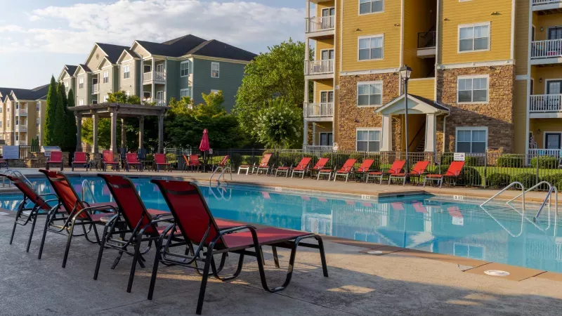 Outdoor swimming pool lined with red lounge chairs, bordered by multi-story apartment buildings.