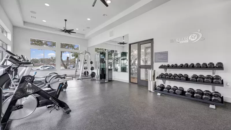 Bright, modern fitness center with treadmills, bikes, weight machines, and a dumbbell rack.