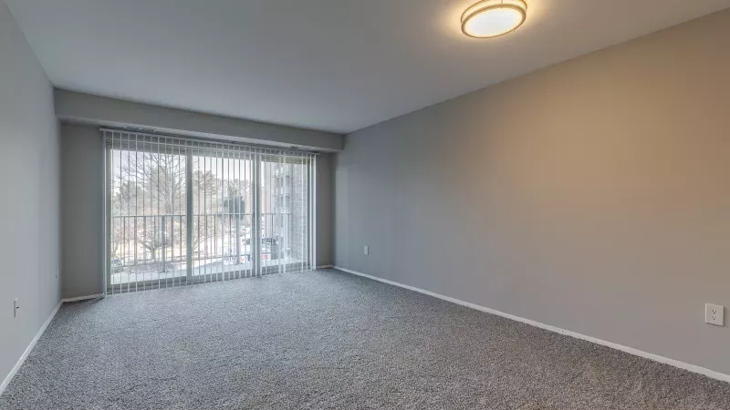 Empty room with light gray walls, gray carpet, and a large sliding glass door leading to a balcony.