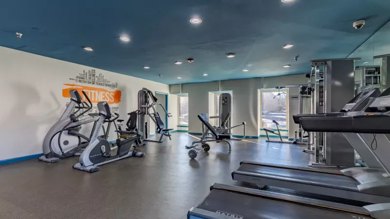 Well-lit fitness center with a blue ceiling, white walls, and various exercise machines including treadmills and ellipticals.