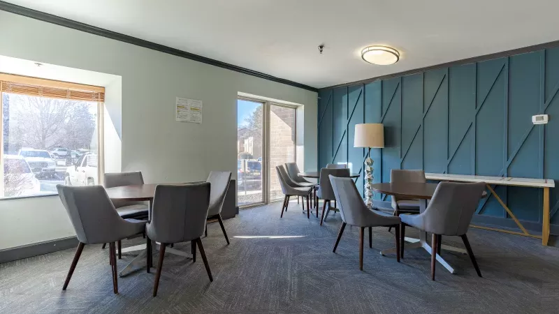 Modern lounge with several round tables and grey chairs, light green walls, and a teal geometric accent wall.