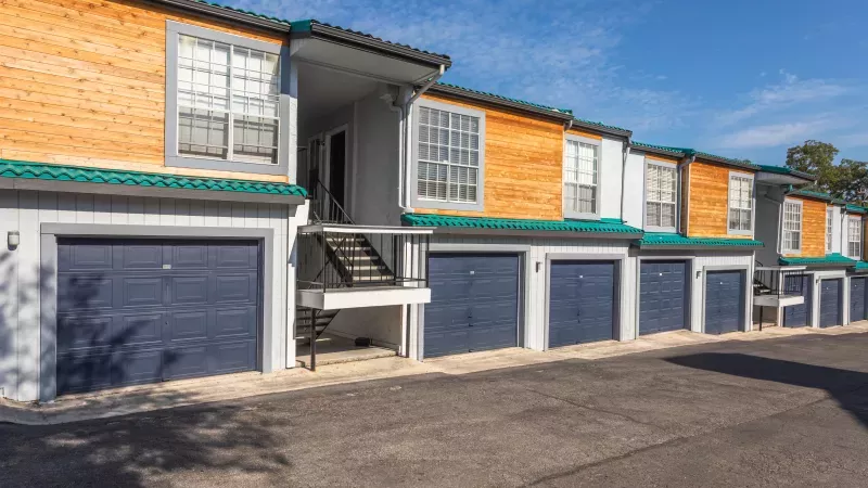 Modern apartment units with blue garage doors, light wood siding, green roof trim, and external stairs.