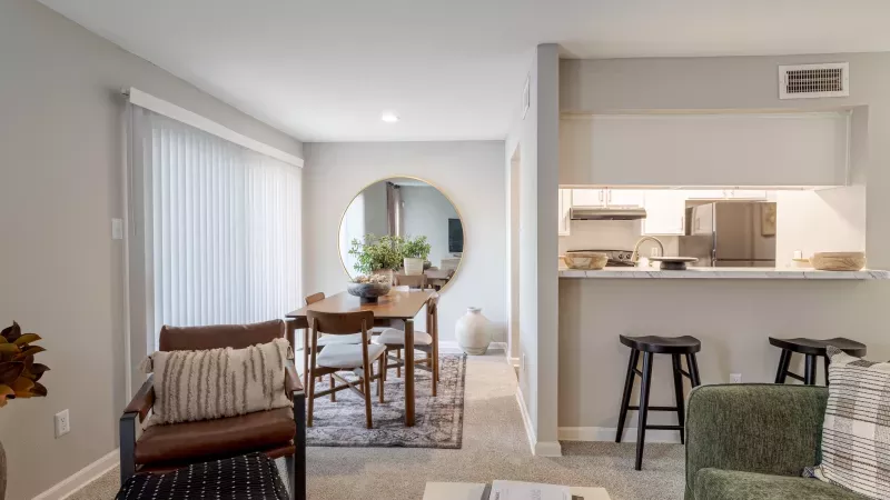 Modern open-plan living room with dining area featuring a round mirror, leading to a kitchen with a breakfast bar.