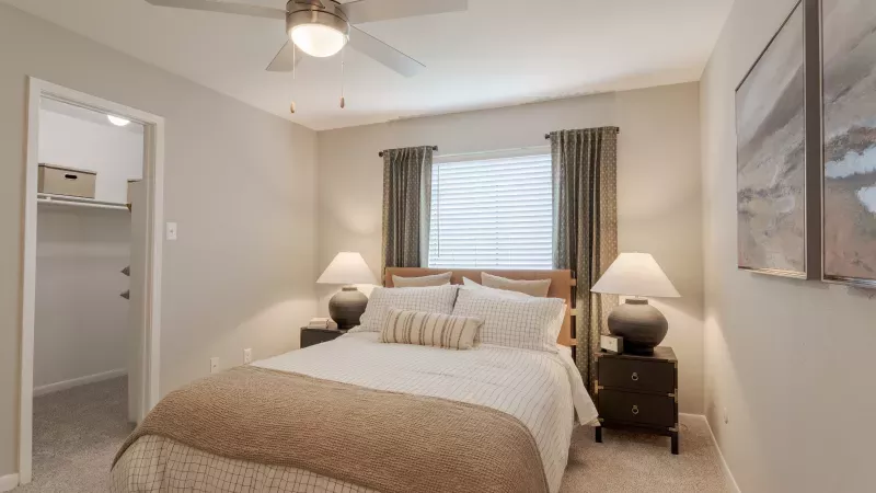 Bedroom with a queen bed, white bedding, brown throw blanket, two nightstands with lamps, and a ceiling fan.