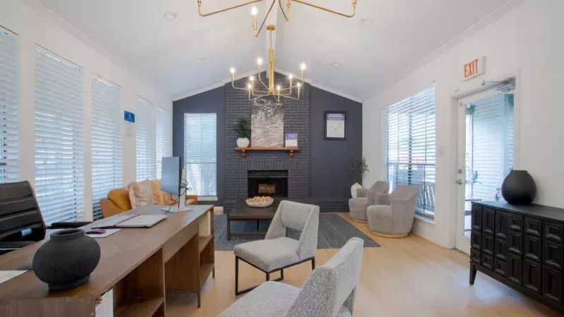 Spacious, modern lounge with vaulted ceiling, geometric chandelier, fireplace, dark blue wall, wooden desk, various chairs.