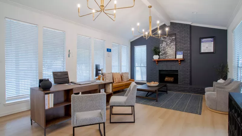Stylish lounge with a desk, seating area, and fireplace. Dark stone facade, navy accent wall, wood floors, and gold chandeliers.