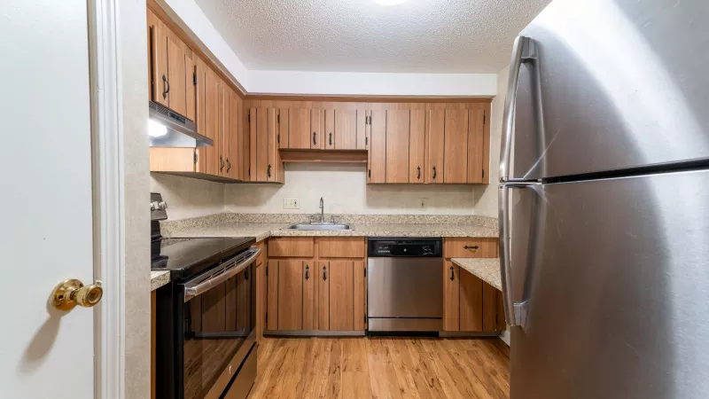 Clean kitchen with light wood cabinets, stainless steel appliances, and a wood floor. Refrigerator on right.
