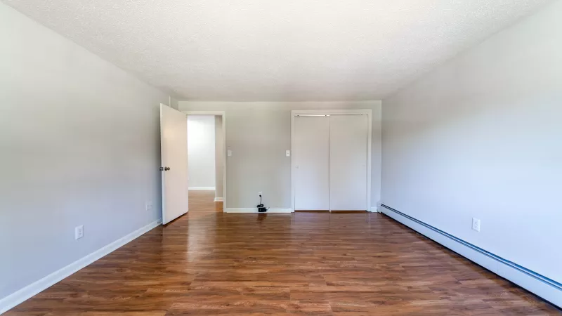 Empty room with light gray walls, wood laminate flooring, an open doorway, closet, and baseboard heater.
