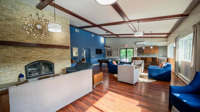 Spacious community lounge with a stone fireplace, wood floors, blue walls, modern seating, and a pool table.