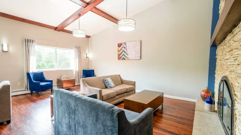Spacious living room with exposed wooden beams, brown and blue sofas, blue armchairs, and a stone fireplace.