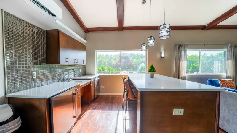 Modern kitchen with dark wood floors, white counters, stainless steel appliances, an island, and exposed ceiling beams.