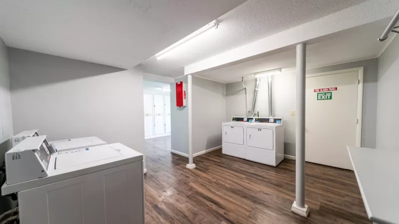 Clean laundry room with multiple white washing machines, dark wood-look flooring, and a utility sink.