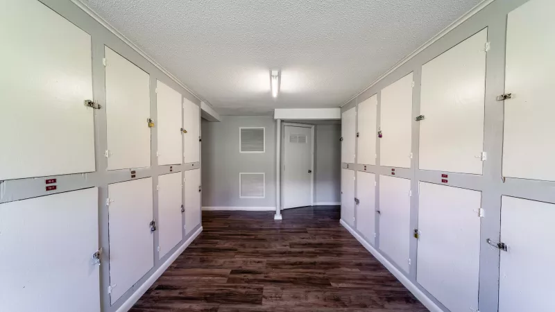 Indoor storage corridor with white locker units, dark wood floor, and fluorescent lighting.