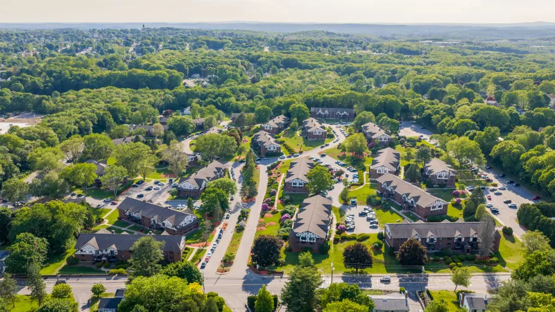 Aerial photograph of a residential community with red-roofed buildings, winding roads, and abundant green trees.