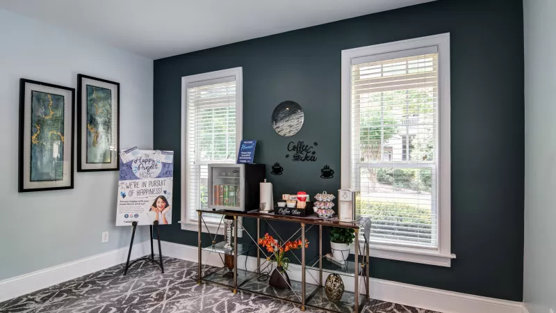 Coffee station with supplies on a metal cart, framed art, and a sign in a room with teal and light blue walls.