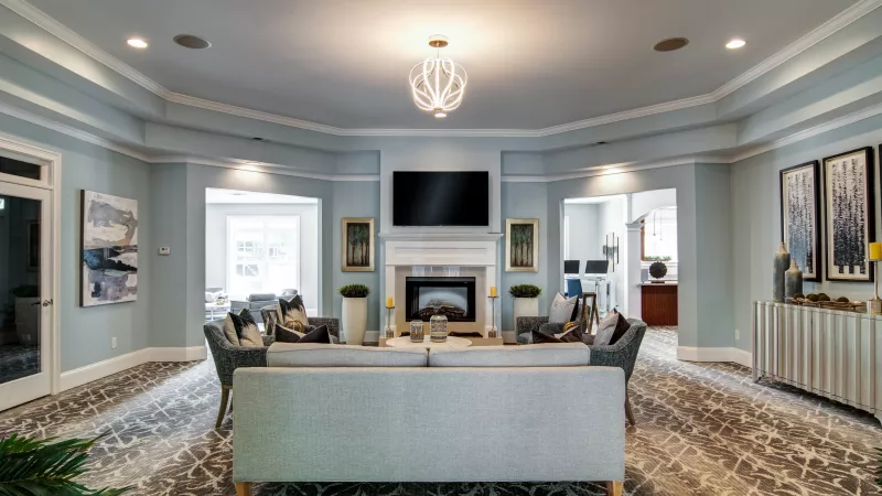 Elegant lounge with light blue walls, a fireplace, TV, and a blue sofa surrounded by armchairs.