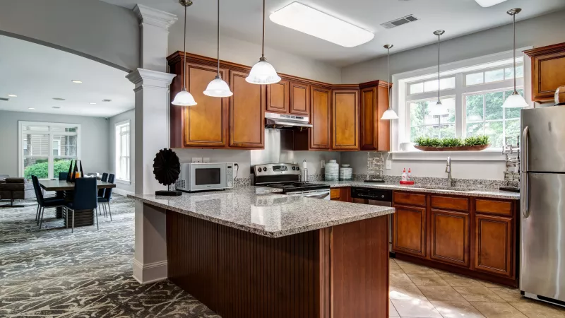 Bright kitchen with warm wood cabinets, granite island, stainless steel appliances, and a dining room visible through an archway.