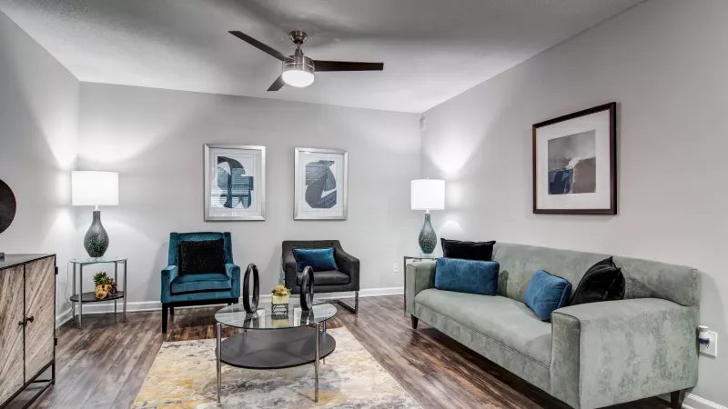Modern living room with a green sofa, blue armchairs, abstract art, dark wood floor, and a yellow and blue patterned rug.