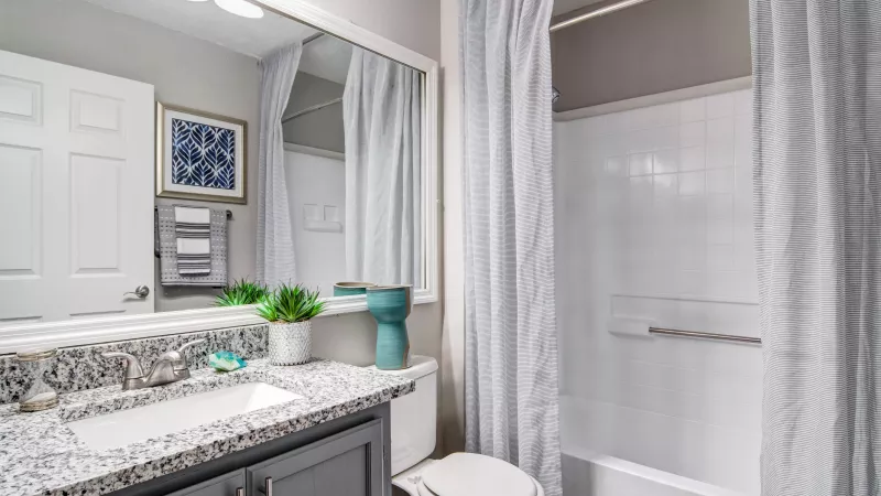 Modern bathroom with a grey vanity, speckled granite counter, large mirror, toilet, and white bathtub with a striped shower curtain.