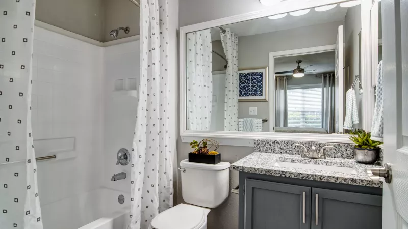 Modern bathroom with white tub, gray vanity, granite counter, and polka dot shower curtain.