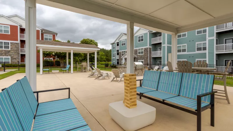 Outdoor apartment patio with blue striped couches, a Jenga game, and lounge chairs. Colorful apartment buildings in background.
