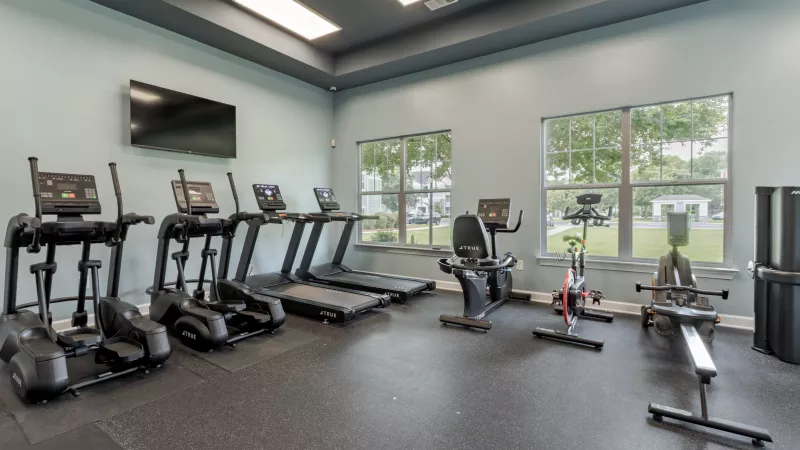 Bright fitness center with light blue walls, rubber floor, and various exercise machines: treadmills, ellipticals, bikes, and a rowing machine.