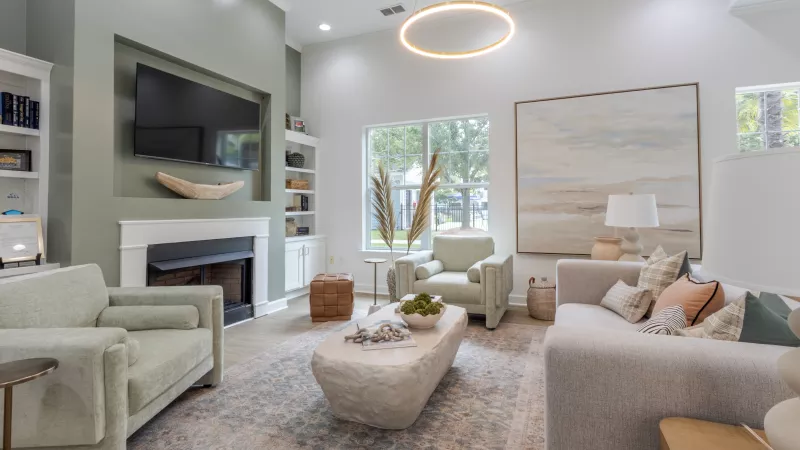 Modern living room with a green accent wall, fireplace, TV, white sofa, light green chairs, and abstract art.