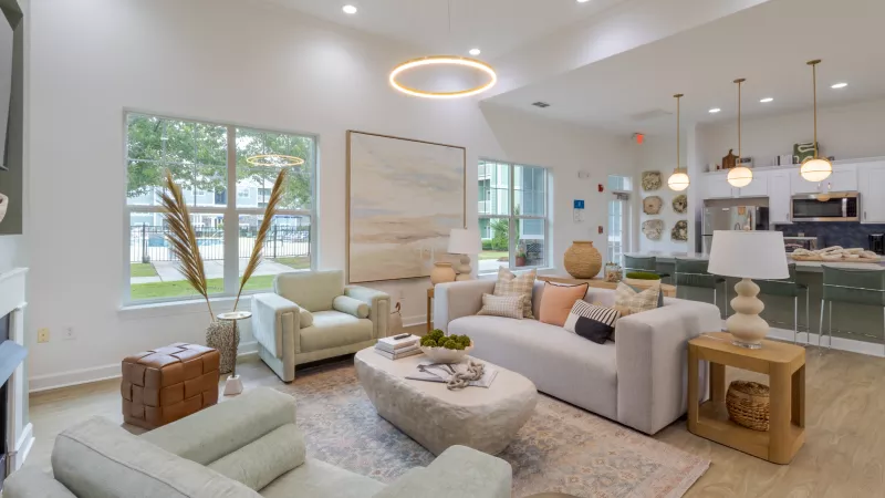 Spacious, bright living area with light gray sofa, green armchairs, textured rug, and large abstract artwork.