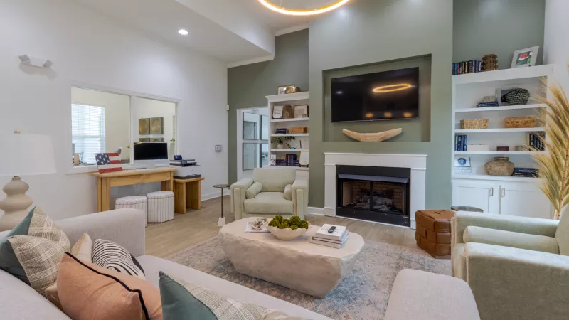 Inviting modern living room with white sofas, a sculptural coffee table, fireplace, TV, built-in shelves, and a sage accent wall.