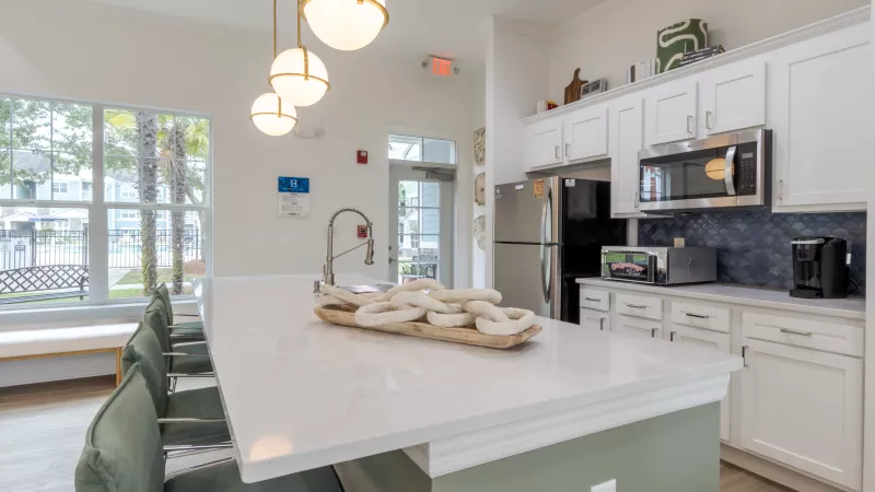 Modern kitchen featuring a white island with green bar stools, white cabinets, stainless steel appliances, and large windows.