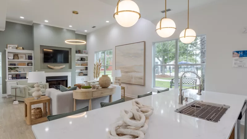 Modern, open-concept living area with white kitchen island, sofa, fireplace, and large windows looking outdoors.