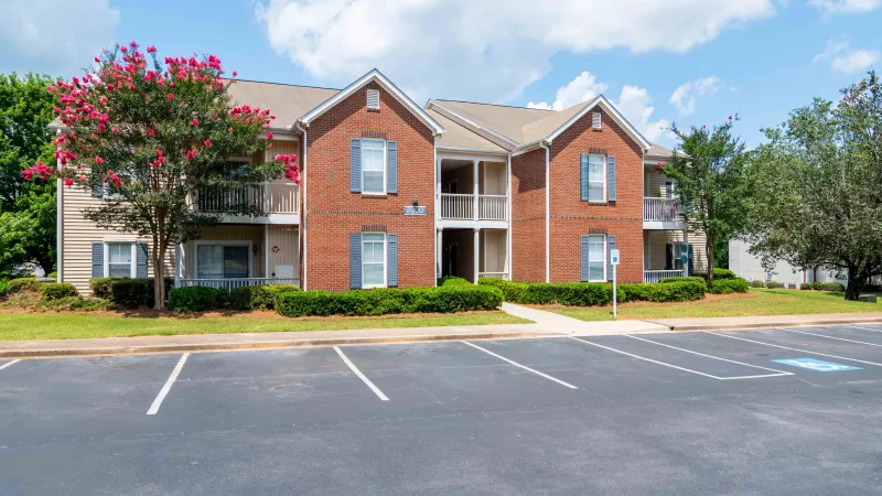 Two-story apartment building, brick and beige, with blue shutters, balconies, and a paved parking lot.