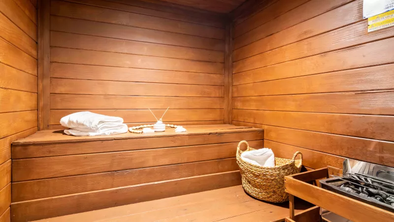 Cozy wooden sauna room with benches, soft white towels, essential oil diffuser, and hot rocks for steaming.
