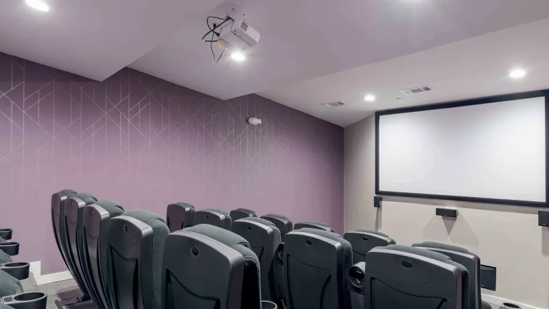 Modern home theater with rows of dark gray recliners, a large screen, and a ceiling-mounted projector.