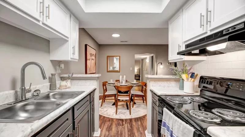 A modern kitchen with marble countertops, dual sinks, and black appliances facing a cozy dining area.