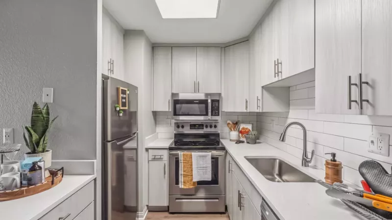 A sleek, modern kitchen featuring stainless steel appliances, white cabinetry, a subway tile backsplash, and bright natural lighting from a skylight.