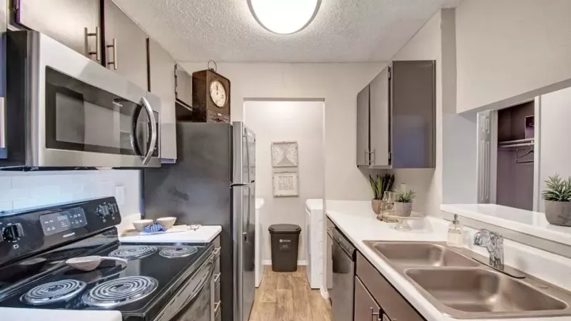 Modern kitchen with stainless steel appliances, including a stove, microwave, and refrigerator, featuring a clean design with white cabinets and dark countertops.