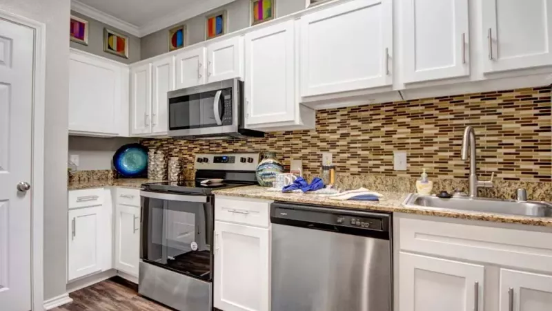 A modern kitchen with white cabinets, stainless steel appliances, granite countertops, and a tiled backsplash.