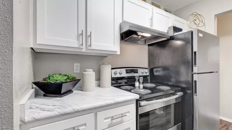 A modern kitchen featuring sleek white cabinetry, marble-style countertops, and stainless steel appliances, including a black oven and refrigerator, complemented by stylish decor accents.