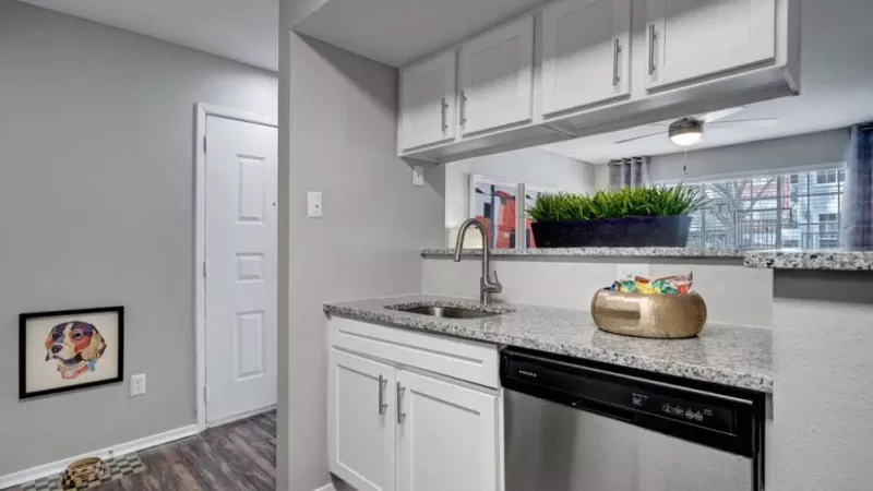 A modern kitchen featuring white cabinets, granite countertops, and stainless steel appliances with a view of the living area.