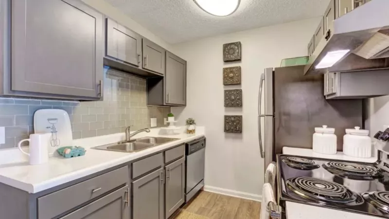 Modern kitchen with gray cabinetry, stainless steel appliances, white countertops, and a tile backsplash in a Residences at West Mint apartment.