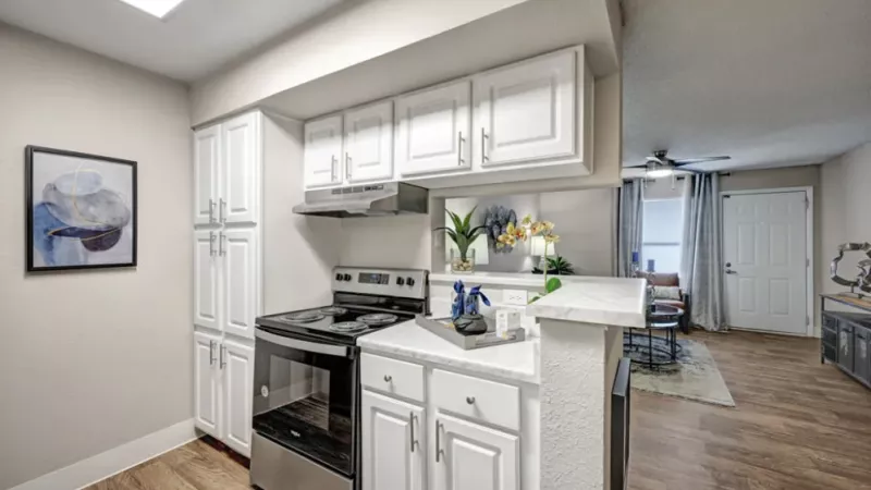 A modern kitchen with sleek white cabinetry, stainless steel appliances, and a view into a cozy living area.