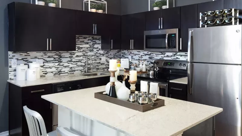 Modern kitchen with dark cabinets, stainless steel appliances, and a decorative backsplash, featuring a white island with candles.