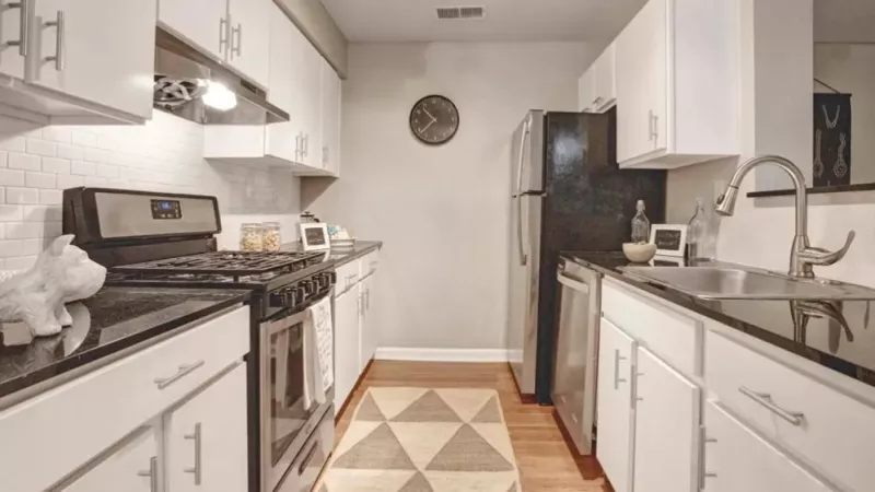 A modern kitchen featuring sleek white cabinets, a stainless steel gas stove, and a stylish subway tile backsplash, complemented by a geometric rug and warm wooden flooring.