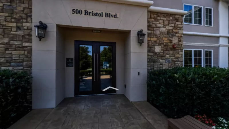  Entrance to The Grove Somerset Apartments, featuring a stone and stucco facade with double glass doors and landscaped greenery for a welcoming entry.
