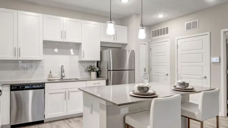 A modern kitchen with white cabinetry, stainless steel appliances, and a large island with two white barstools.