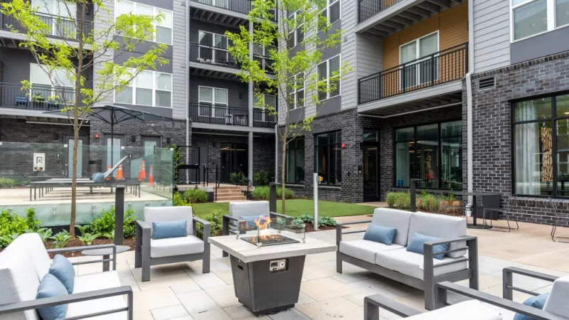 An inviting outdoor courtyard with a fire pit, modern lounge seating, and lush greenery, creating the perfect space for socializing and unwinding.