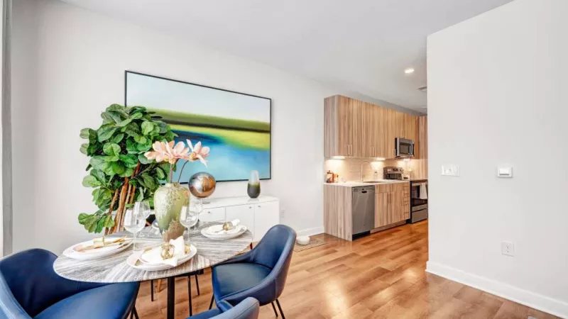 A beautifully set dining table with plush blue chairs, positioned next to a contemporary kitchen with wood-finish cabinets and stainless-steel appliances.